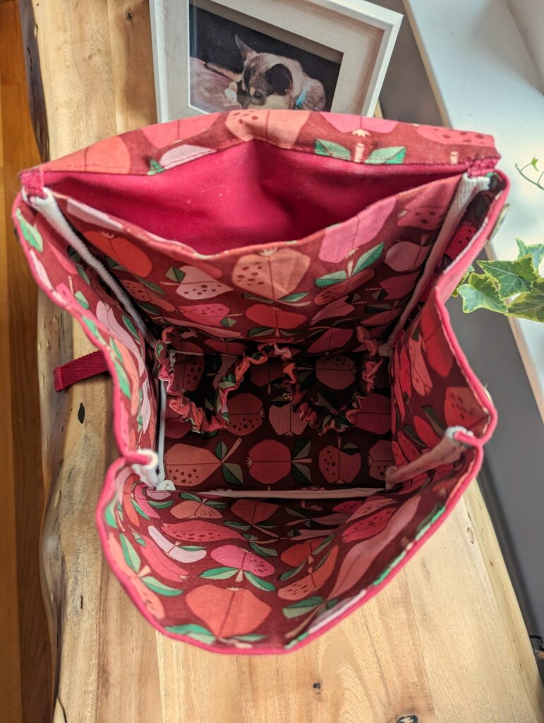 View inside red toddler backpack. There's a thin full-size pocket at the back, and a big open pocket with two elastic scrunchie things in it to hold contents still.