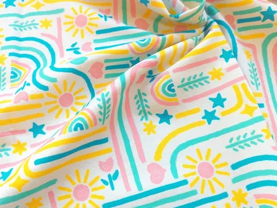 Canvas fabric with bright pink, yellow, blue, and green hand-drawn patterns folded up and stacked on matching solid color canvas.