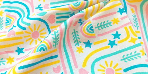 Canvas fabric with bright pink, yellow, blue, and green hand-drawn patterns folded up and stacked on matching solid color canvas.