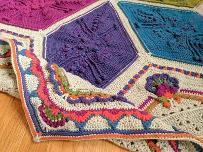 Close up image of an Ubuntu crochet blanket, folded so that the border is visible next to the middle, showing off the two flower like parts of the design.