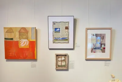 Photograph of a wall in a gallery, showing four artworks hanging on a white wall. The one at top center is "Attachment", the subject of this blog post, in a white mat and narrow black frame.