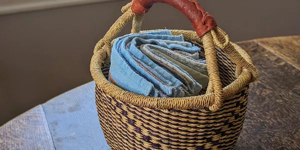 A collection of white and blue cotton dish towels sitting in a basket on top of a wooden table.
