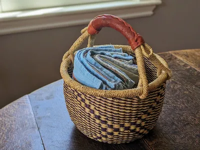 A collection of white and blue cotton dish towels sitting in a basket on top of a wooden table.
