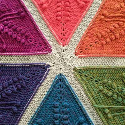 Close up image of the center of an Ubuntu crochet blanket, where the points of 6 diamond shapes meet. The diamonds are different bright colors (magenta, salmon, orange, green, blue, purple) and there is a light gray border between them.