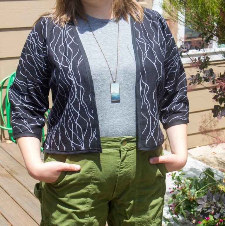 Picture of a person wearing a boxy, open front jacket over clothes that aren't relevant to the post. The jacket is made from a lightweight canvas that is black with a printed pattern of zig-zagging white lines over it.