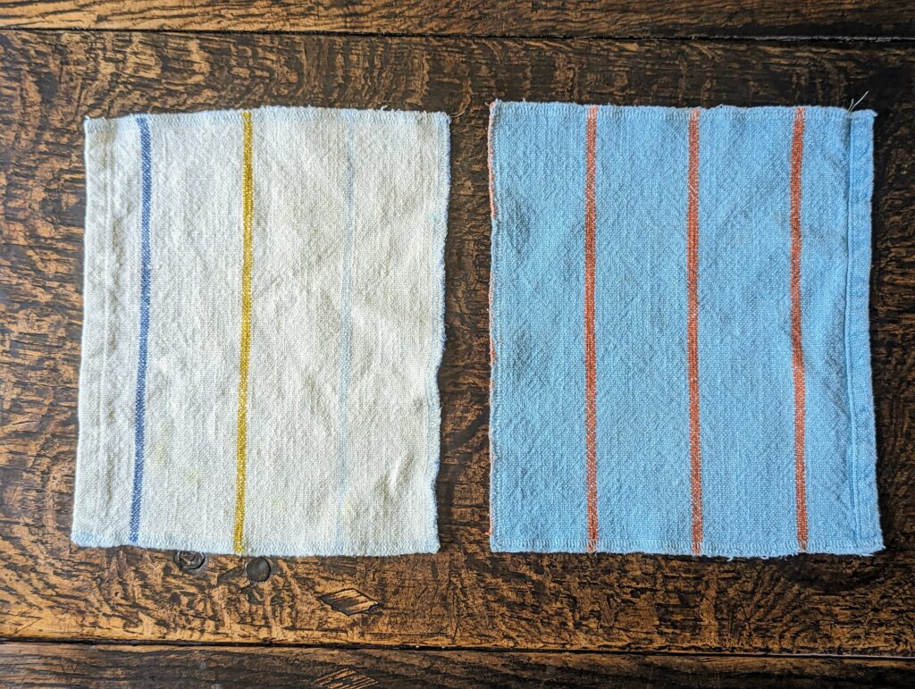 Two cotton dish towels lying flat on a table. One is white with navy, mustard, and light blue stripes, the other is light blue with orange stripes.